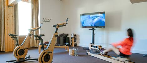 Un gimnasio en casa con bicicletas estáticas, una máquina de remo y un televisor en la pared.