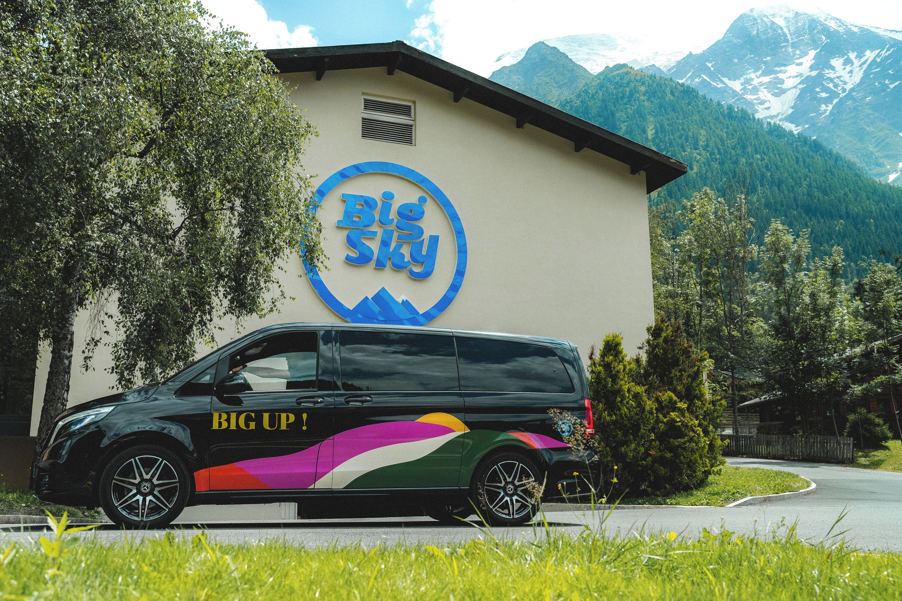 A van parked in front of a building with a 'Big Sky' sign, surrounded by greenery and mountains.