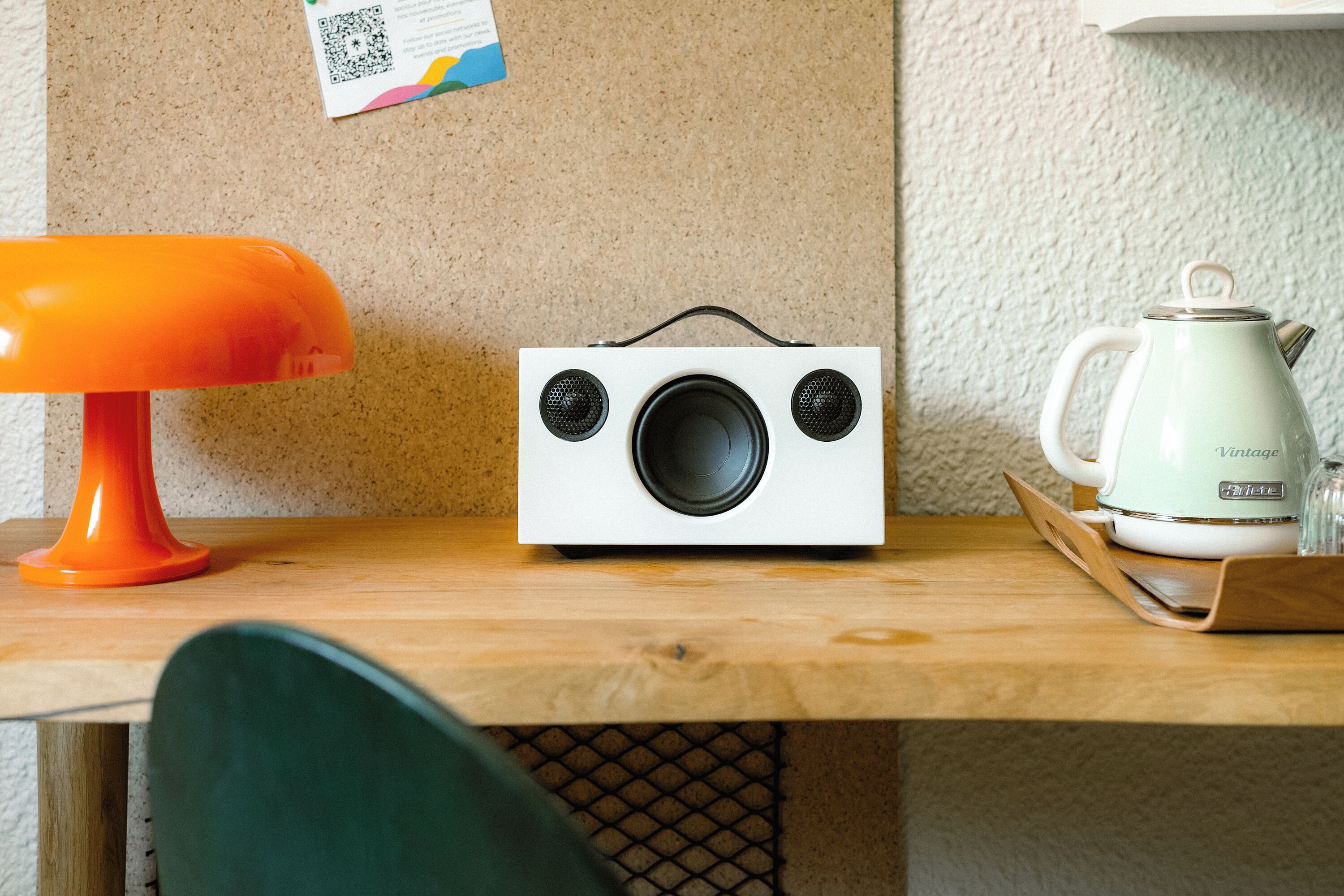 A wooden table with a white radio, a green chair, and a white kettle on a tray.