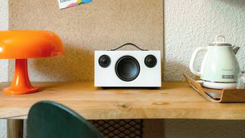 A wooden table with a white radio, a green chair, and a white kettle on a tray.