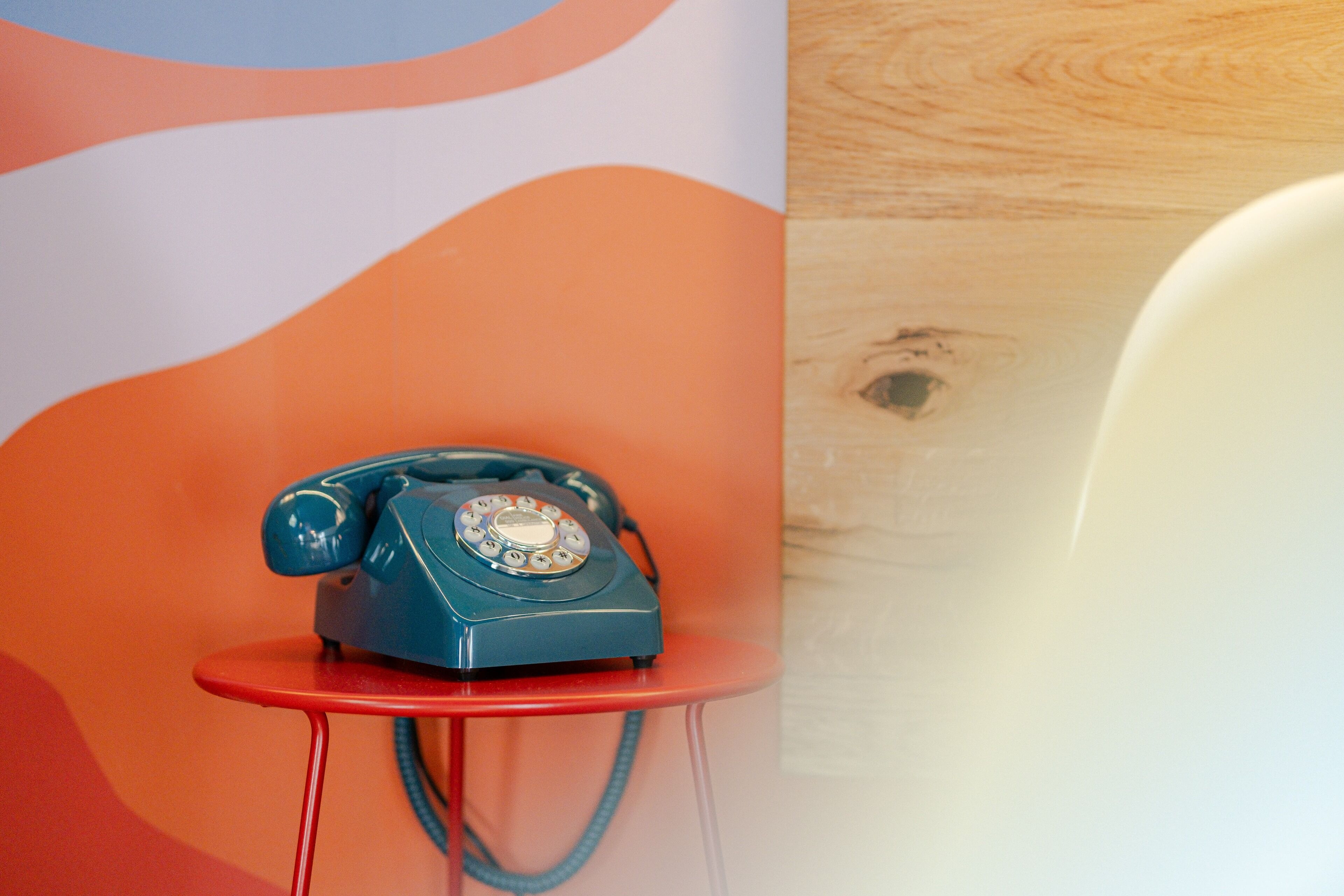 A blue rotary phone on a red table against a wall with abstract orange and white patterns.