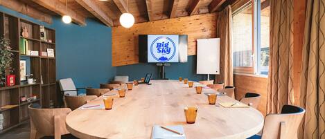 Una sala de conferencias con una mesa redonda, sillas, una pantalla de televisión y una pizarra.