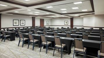 A conference room with multiple rows of tables and chairs, framed pictures on the walls, and a patterned carpet.