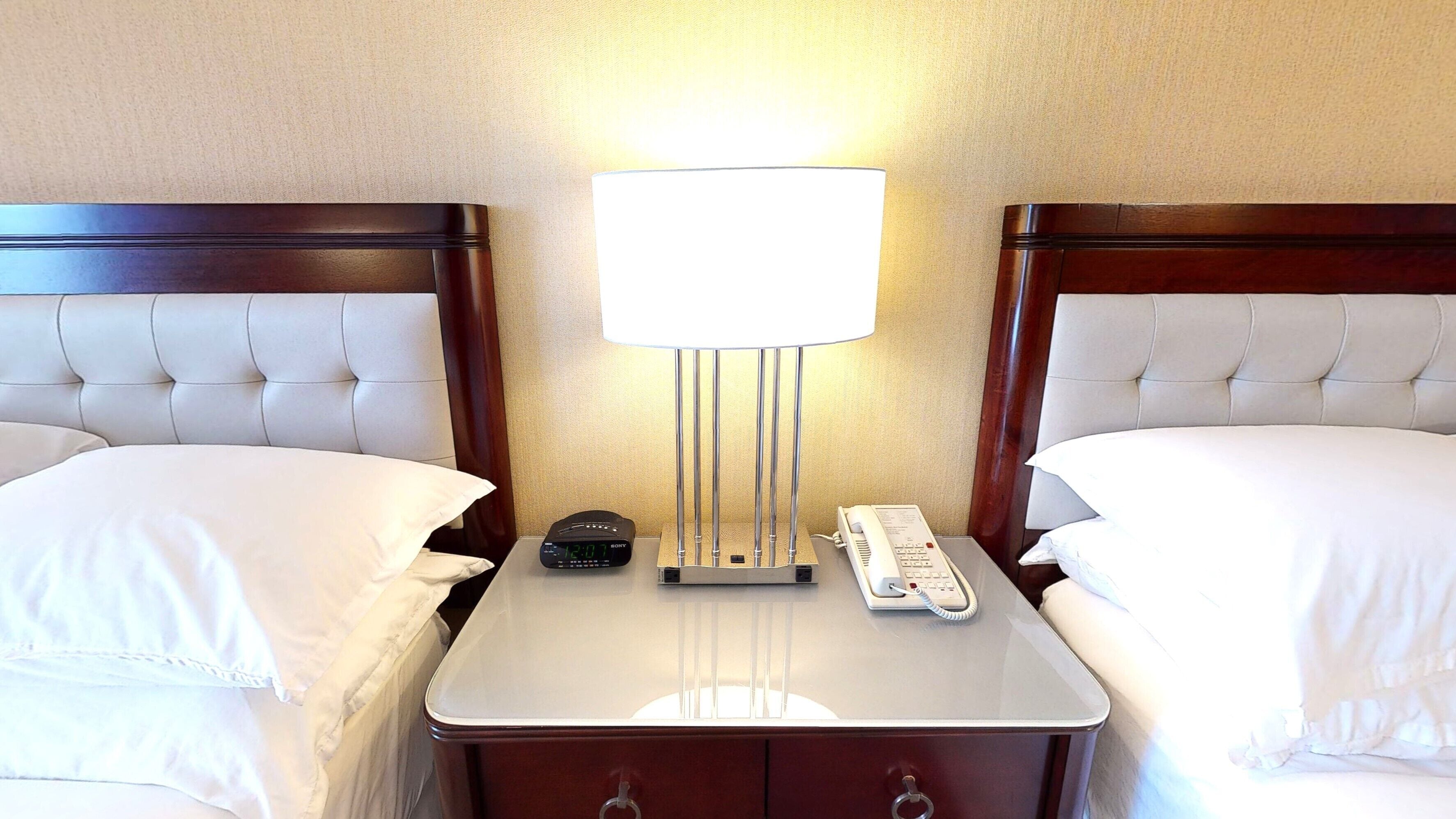 Une chambre d’hôtel avec deux lits, une table de chevet avec une lampe, une horloge et un téléphone.