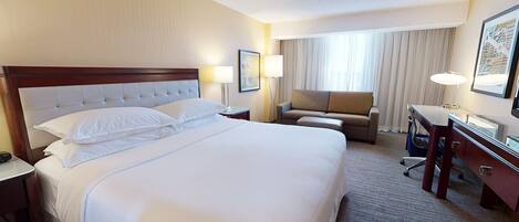 A hotel room with a large bed, a desk, a chair, and a window with curtains.