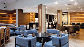 Un salón moderno con sillones de estampado azul, una mesa redonda central y una zona de bar con una cascada.