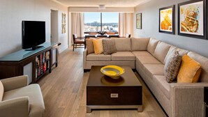 Una sala de estar moderna con sofá, mesa de centro y televisor. Hay cuadros enmarcados en la pared y una vista de la ciudad a través de amplias ventanas.
