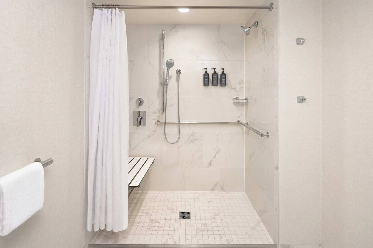 A modern shower area with a glass door, a white towel, and a shelf with toiletries.
