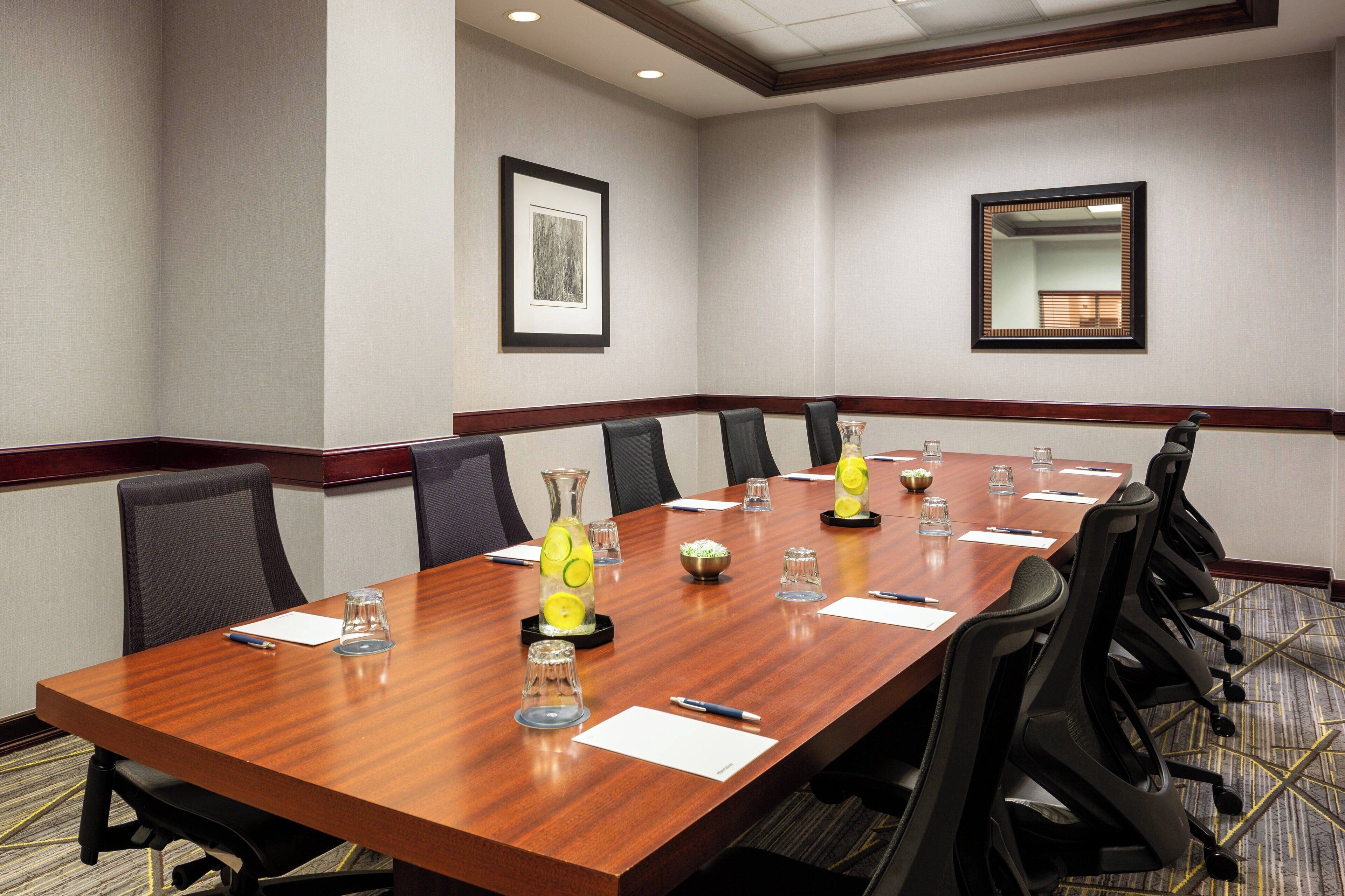A conference room with a long wooden table, black chairs, and a framed picture on the wall.