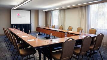 A conference room with a long table, chairs, a projector screen, and a large window with curtains.