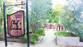 Une enseigne en bois indiquant « Le jardin du chef du Crimson Tavern », avec un chemin menant à un espace de restauration en plein air.