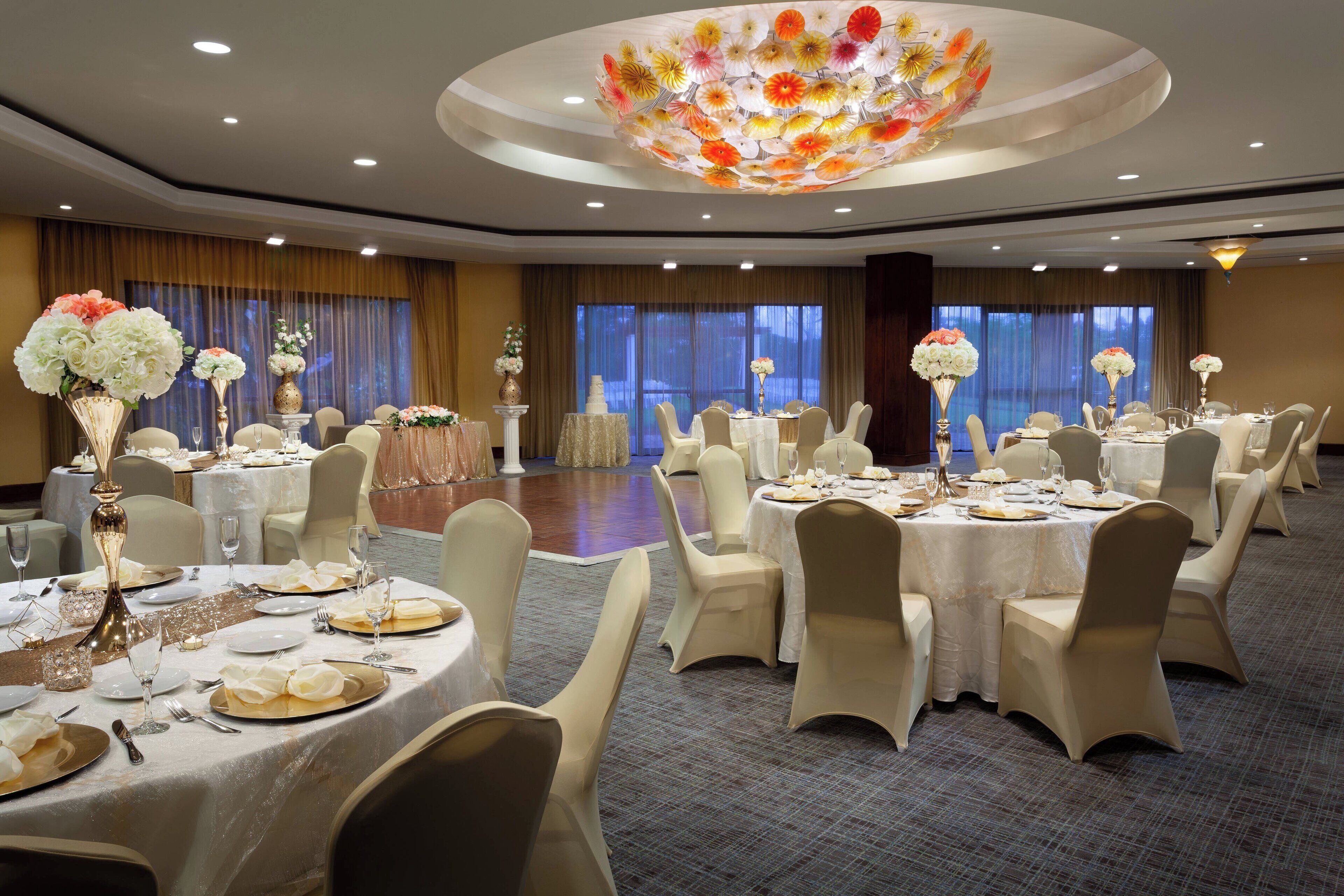 Une salle de banquet avec des tables rondes dressées pour le repas, chacune étant recouverte d’une nappe blanche et agrémentée de chaises assorties.