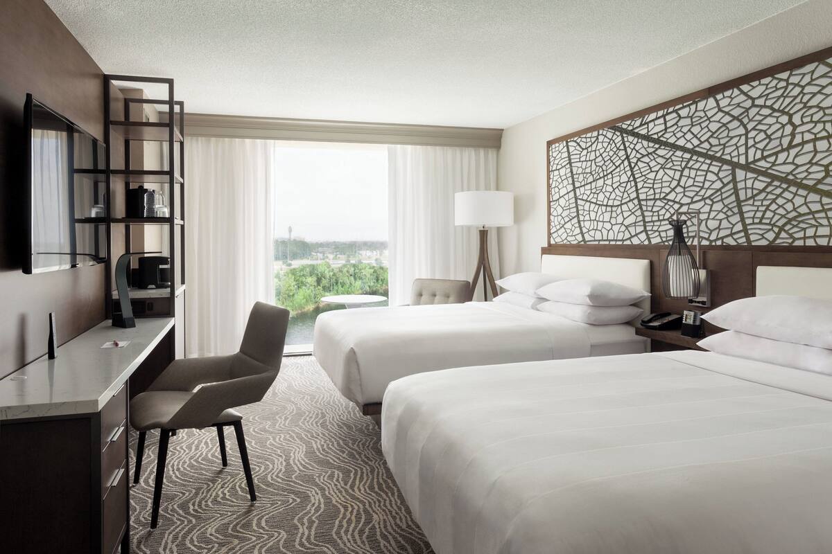 Une chambre d’hôtel avec deux lits, un bureau, une chaise, une lampe et une vue sur la ville.