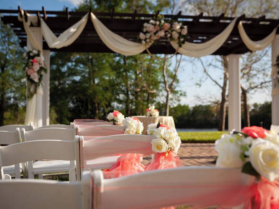 Preparação para uma cerimônia de casamento, com cadeiras brancas e decoração floral.
