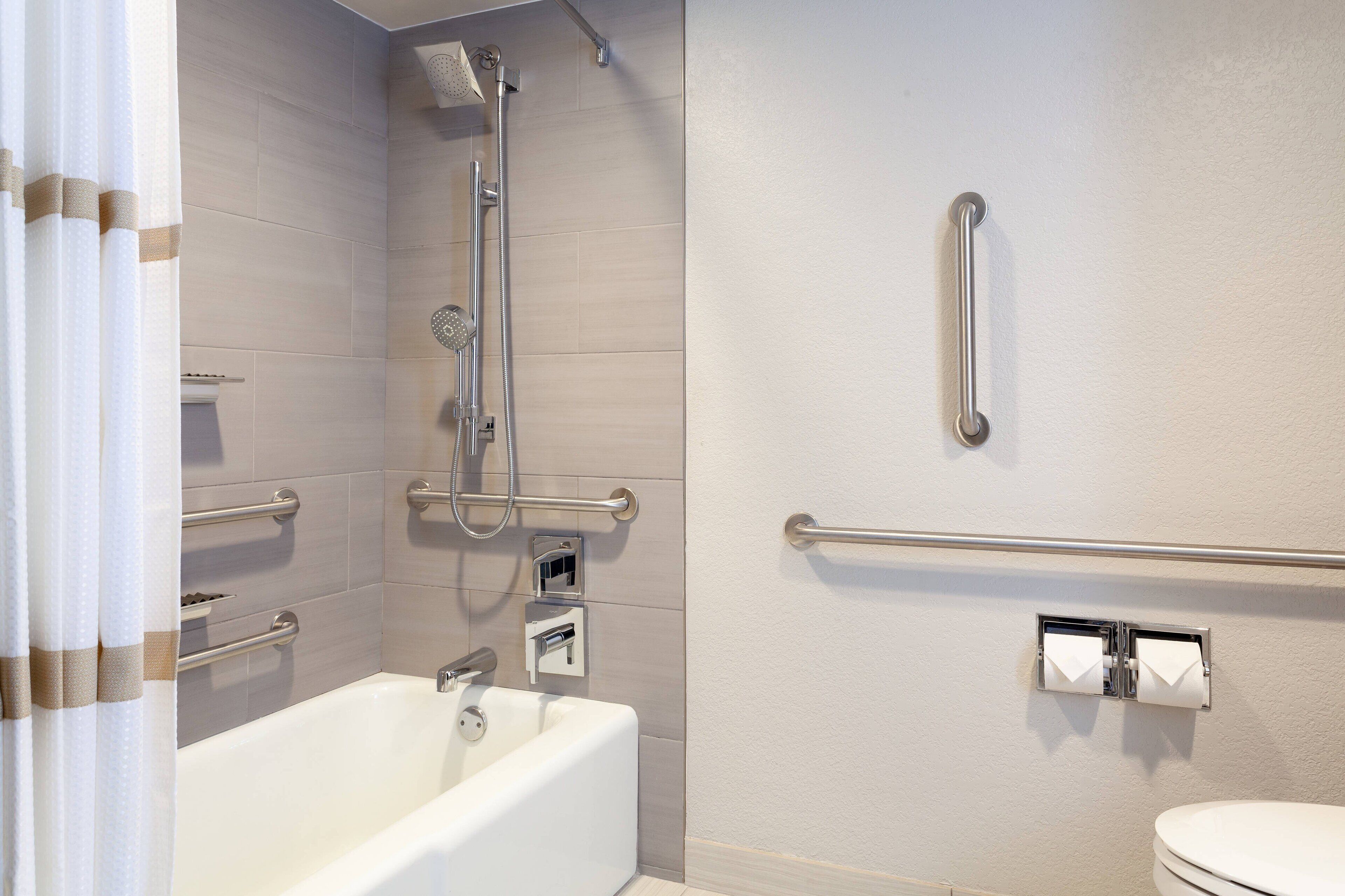 Een badkamer met een bad, een douche en een toilet. Er zijn veiligheidsstangen aangebracht.