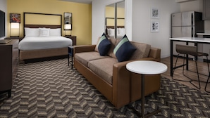 Habitación de hotel con cama, sofá, una pequeña mesa redonda, escritorio y kitchenette.