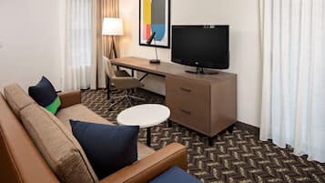 A hotel room with a sofa, a desk, a television, and a small table.