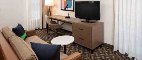A hotel room with a sofa, a desk, a television, and a small table.