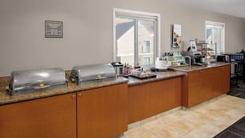 Una zona de cocina con mesas de buffet, que incluye una parrilla, máquina de café y diferentes alimentos.