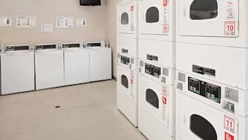 A laundry facility with multiple washing machines and dryers, a television mounted on the wall, and informational posters on the wall.