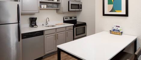 Una cocina moderna con electrodomésticos de acero inoxidable, una encimera blanca y un comedor con mesa y sillas.