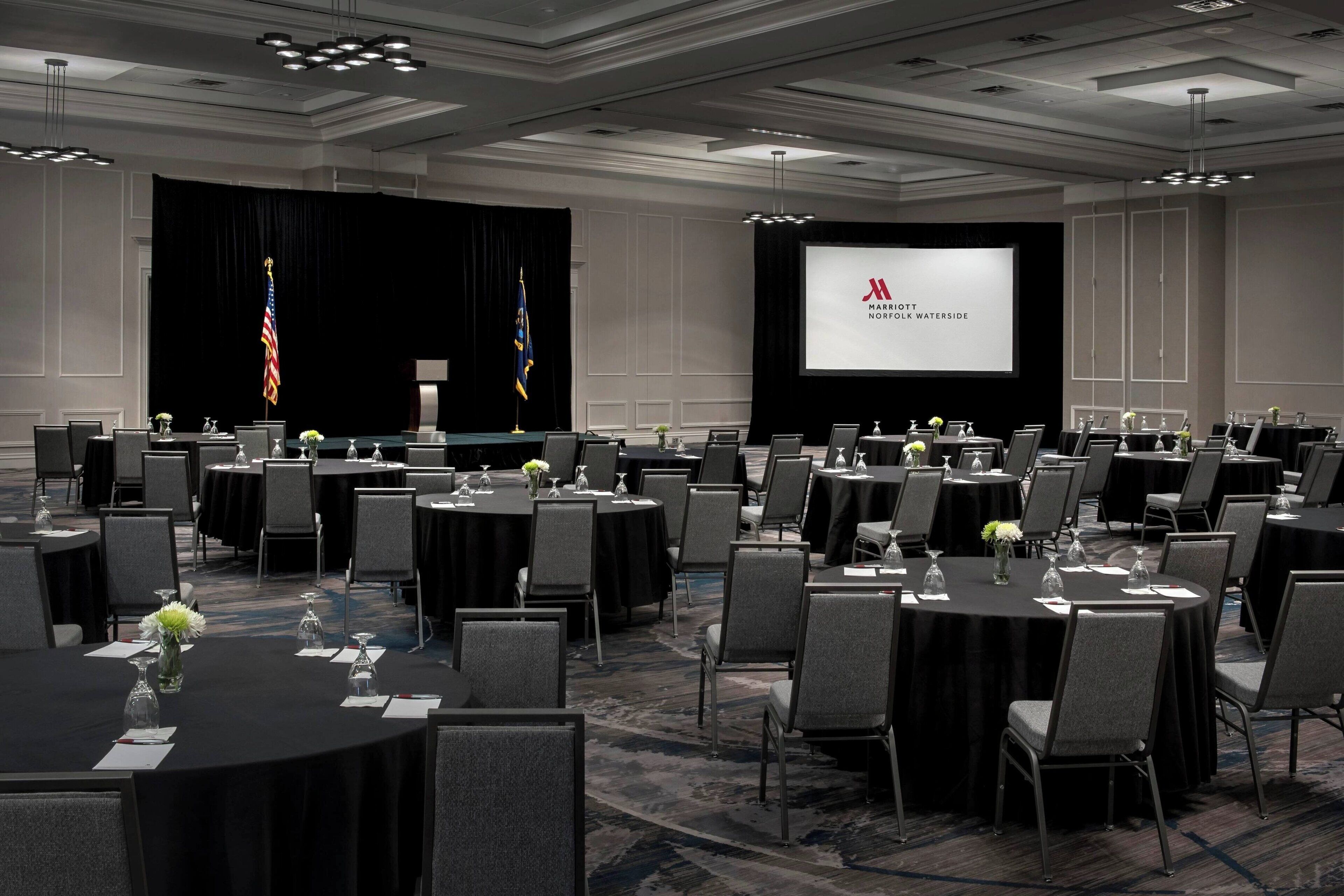 A conference room with multiple round tables, chairs, and a large screen displaying the Marriott logo.