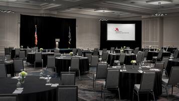 A conference room with multiple round tables, chairs, and a large screen displaying the Marriott logo.