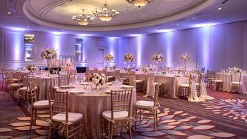 A banquet hall with round tables, gold chairs, and floral centerpieces.