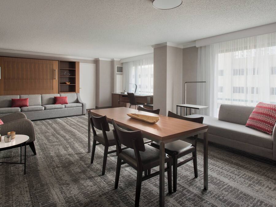 Une chambre d’hôtel moderne dotée d’un coin repas, d’un canapé et d’une grande fenêtre avec des rideaux.
