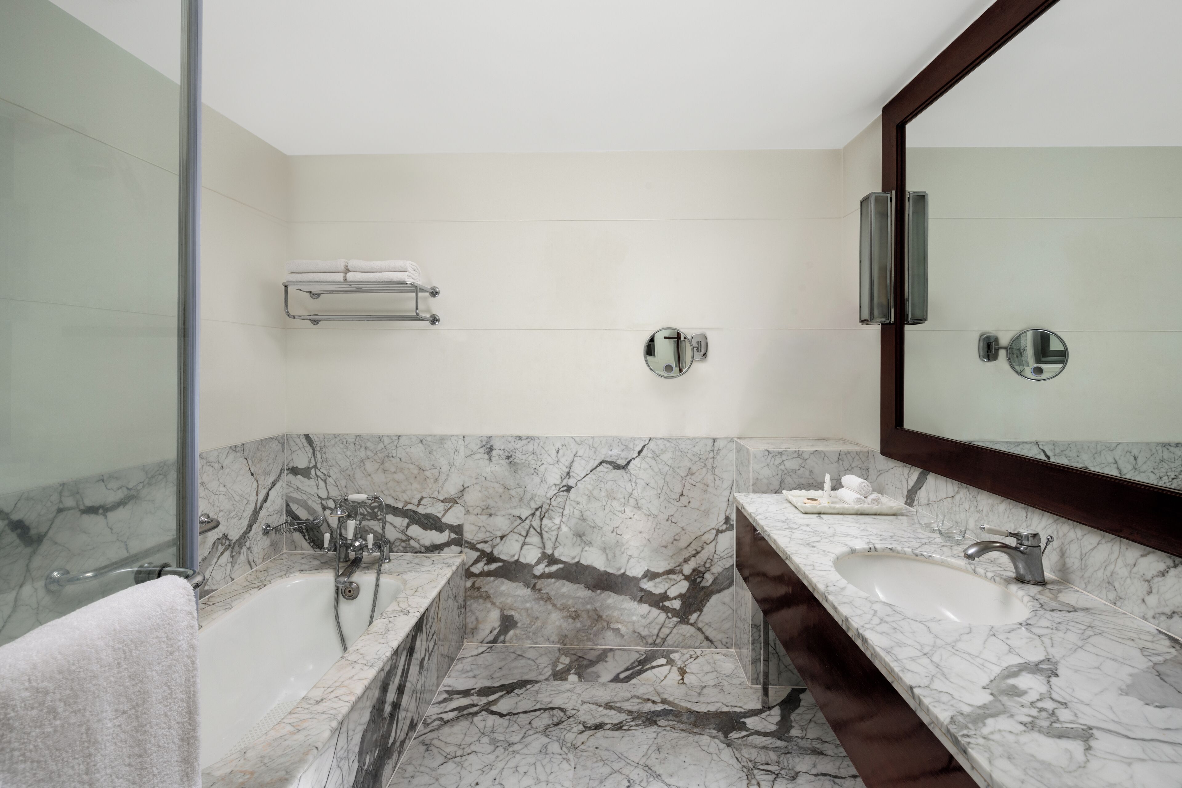 A modern bathroom with a marble vanity, a large mirror, and a glass shower enclosure.