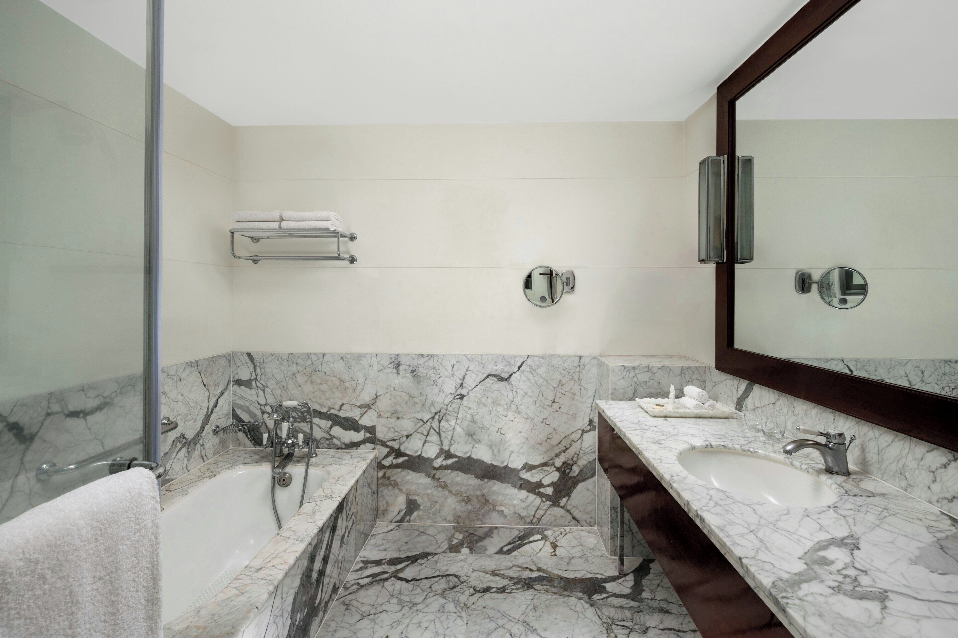 A modern bathroom with a marble vanity, a bathtub, and a large mirror.