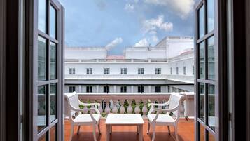 Vista desde un balcón con sillas y una mesa blancos, con vista a un patio con edificios blancos y cielo despejado.