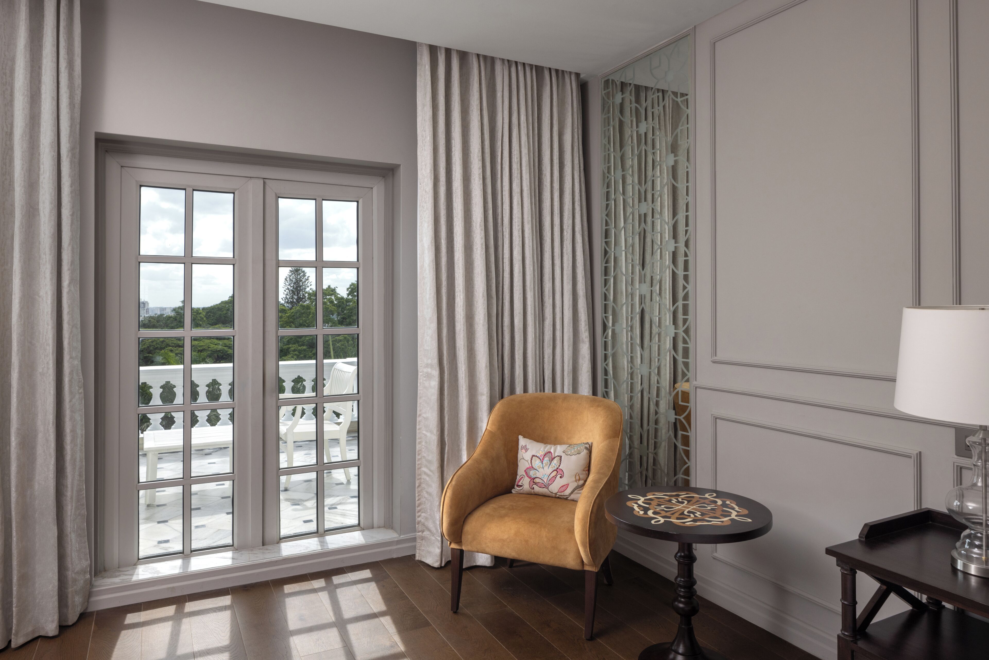 Una habitación con un ventanal grande, una silla, una mesita y una lámpara.