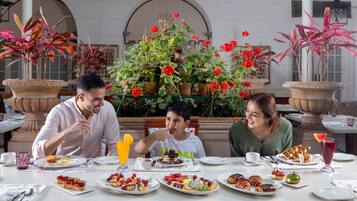 A dining table with various dishes and drinks, surrounded by potted plants and a decorative backdrop.