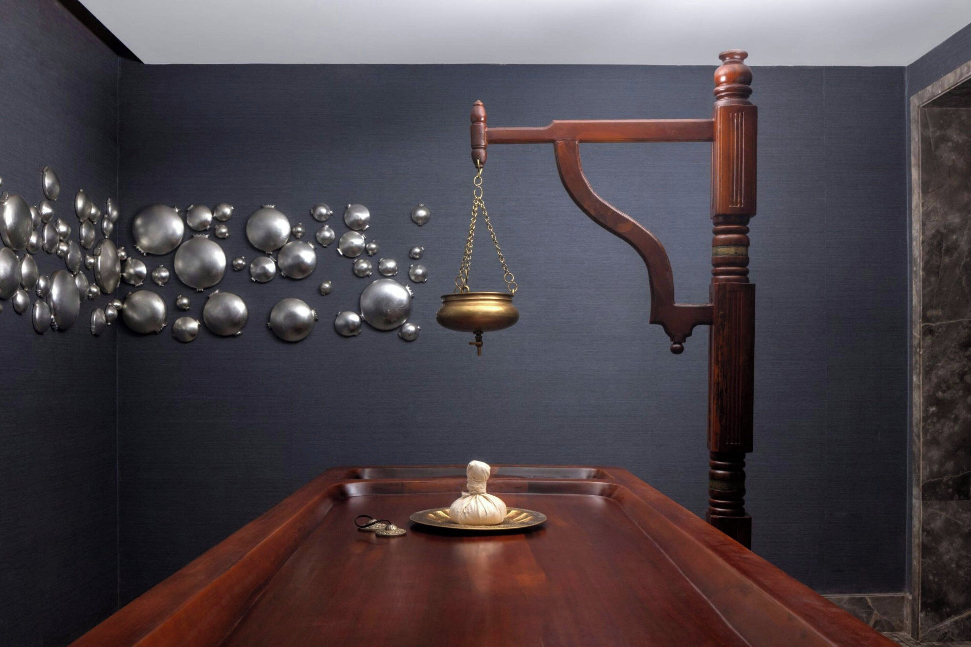 A room with a wooden table, a scale, and a wall with hanging metallic spheres.