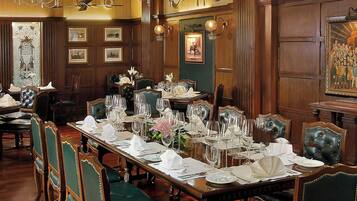A formal dining room with a long table set for a meal, surrounded by upholstered chairs.