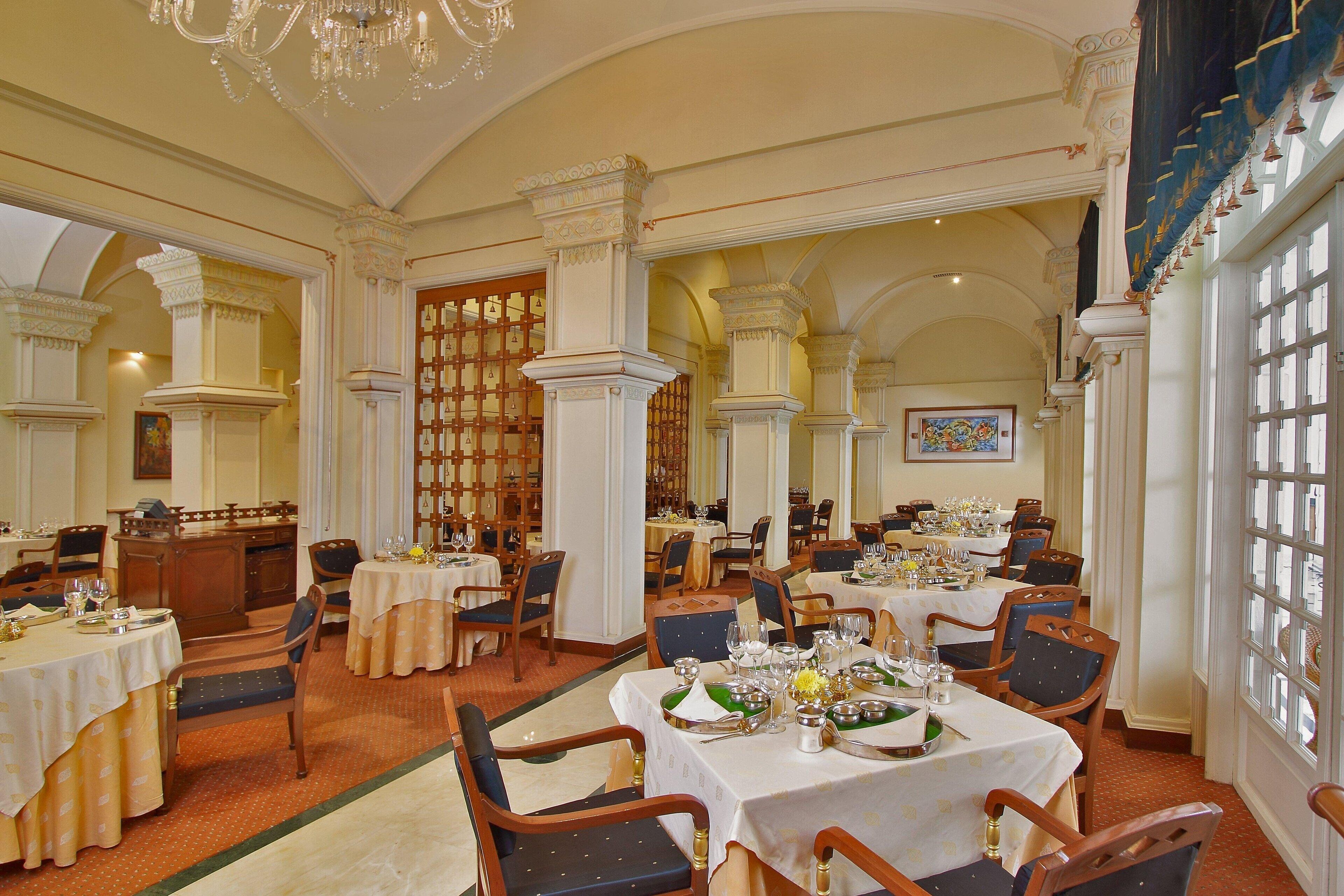 A formal dining room with multiple tables set for service, elegant chairs, and classic architectural details like columns and arches.
