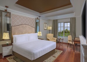 A hotel room with a large bed, two chairs, a small table, a window with curtains, and a mirror with a patterned wallpaper.