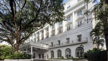 Un edificio blanco y majestuoso con un vestíbulo cubierto, ventanas amplias y un árbol en primer plano.