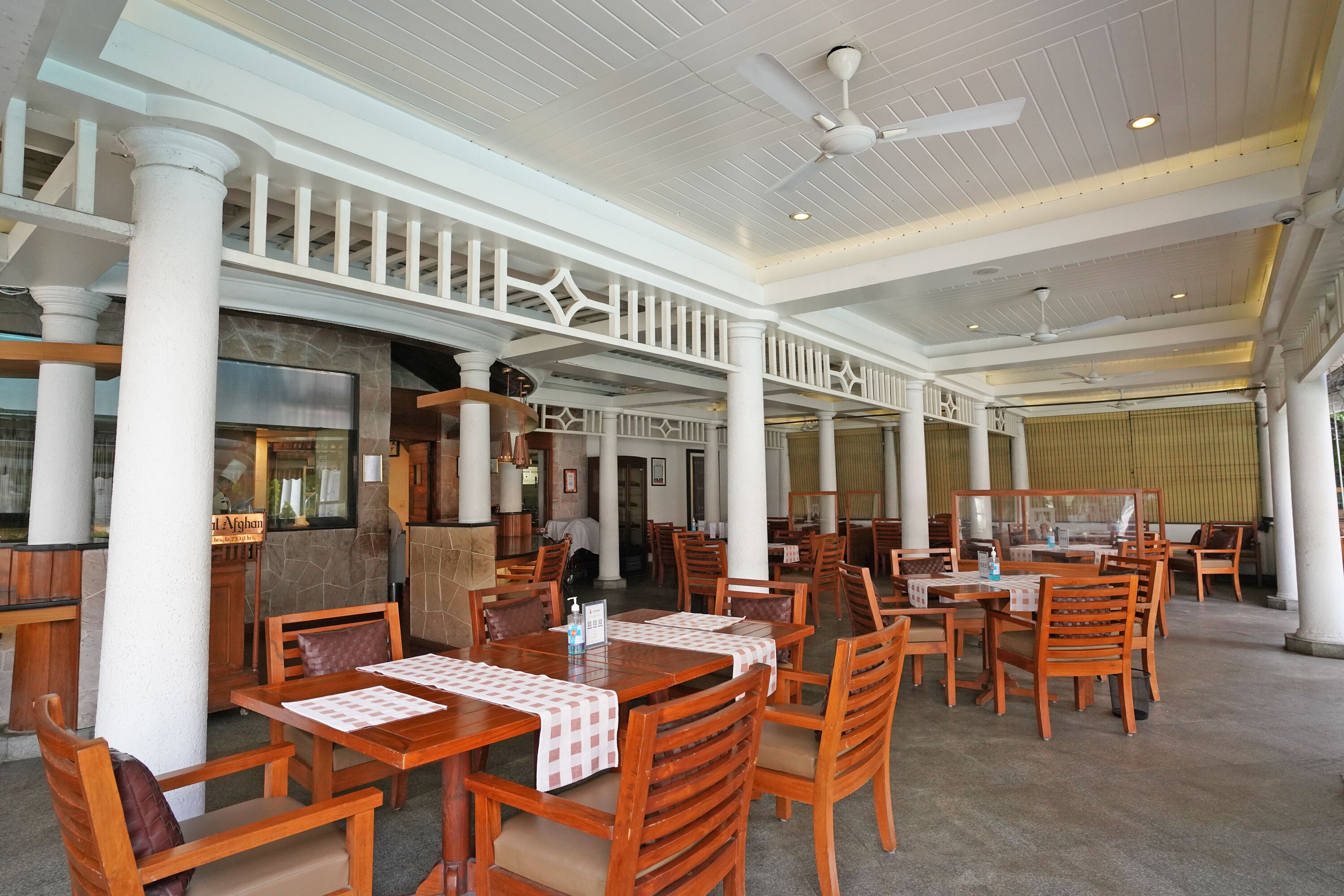 A spacious restaurant with wooden tables and chairs, white columns, and a high ceiling with ceiling fans.