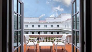 Un balcón con sillas y una mesa blancos, con vistas a un patio con edificios blancos y un cielo despejado.