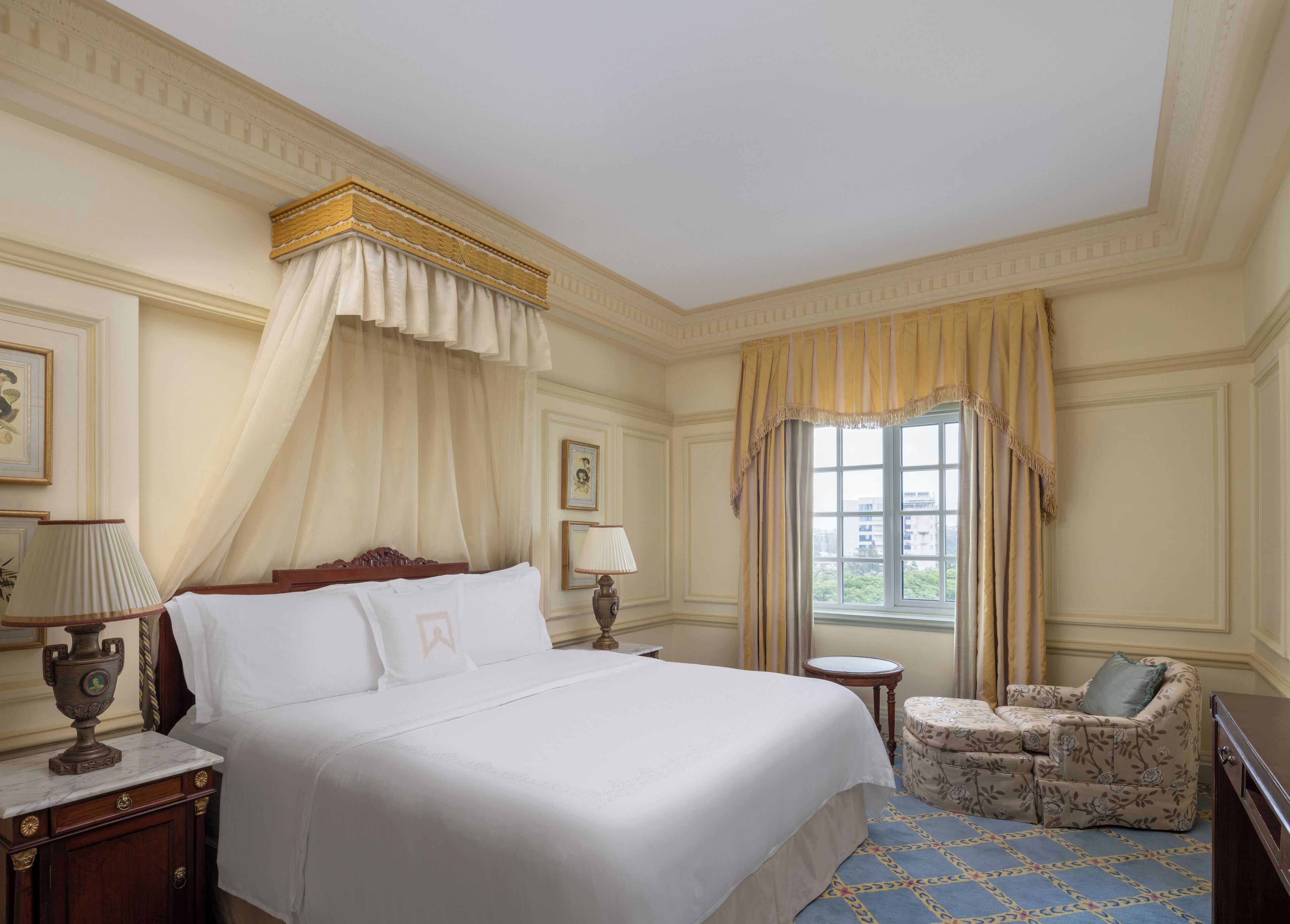 A hotel room with a large bed, a small round table, a sofa, and a window with curtains.