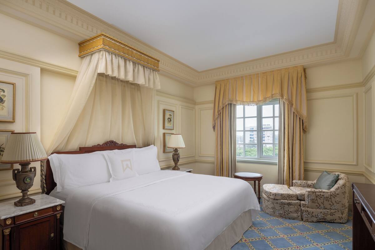 A hotel room with a large bed, a small round table, a sofa, and a window with curtains.