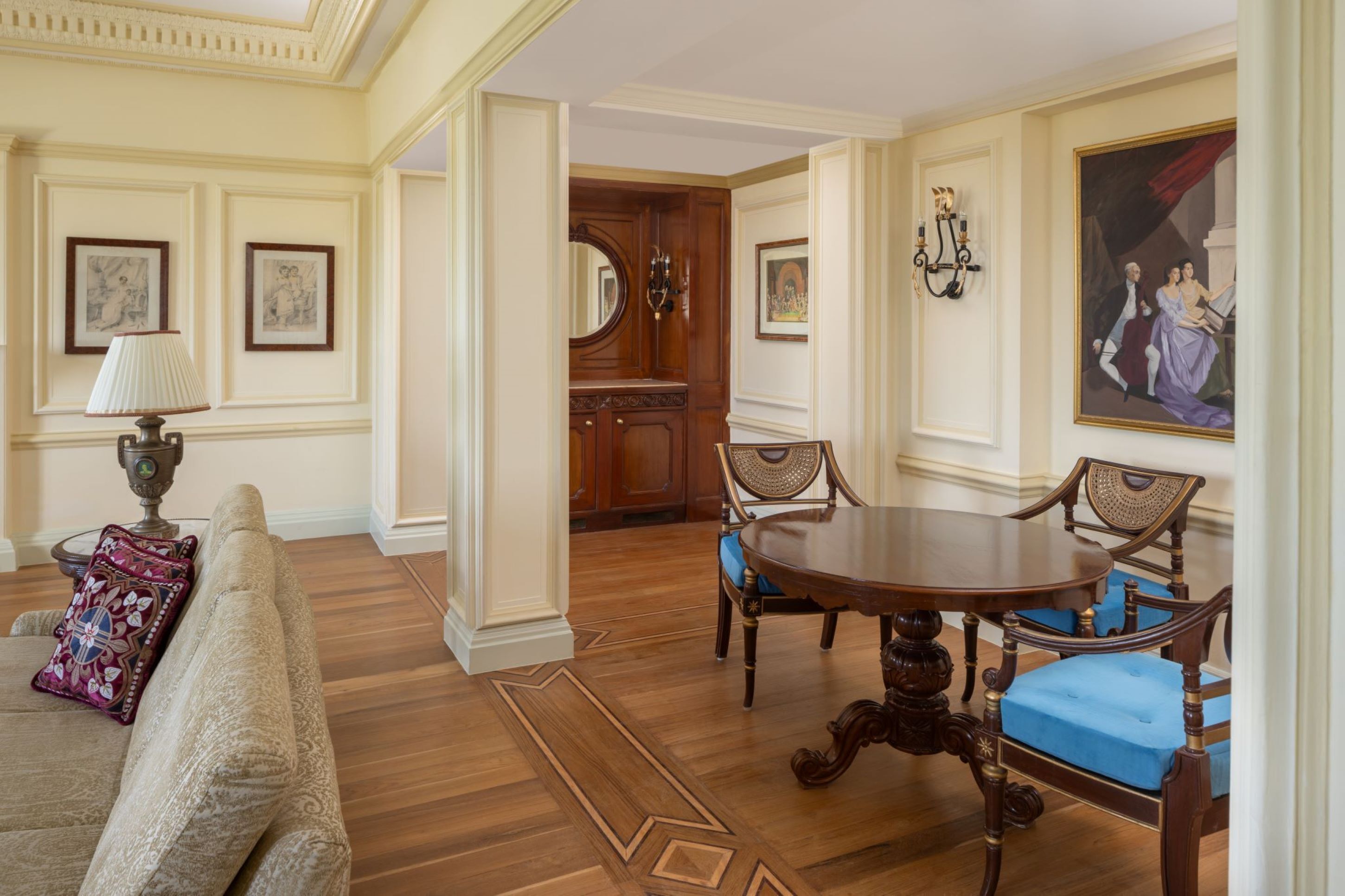 A formal dining room with a wooden table and chairs, a sofa with patterned cushions, and framed artwork on the walls.