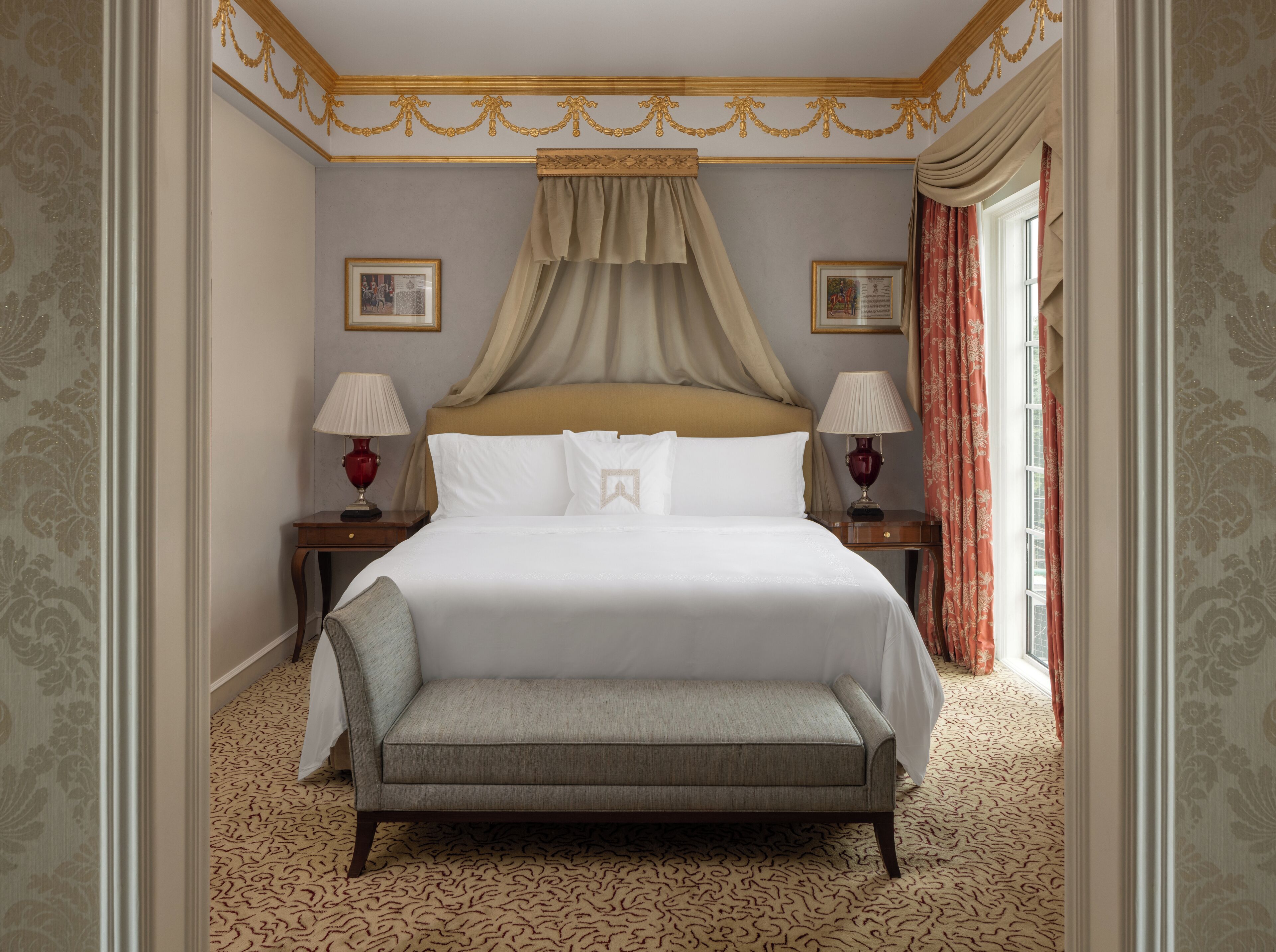 A hotel room with a large bed, two bedside tables with lamps, a bench, and patterned carpet.