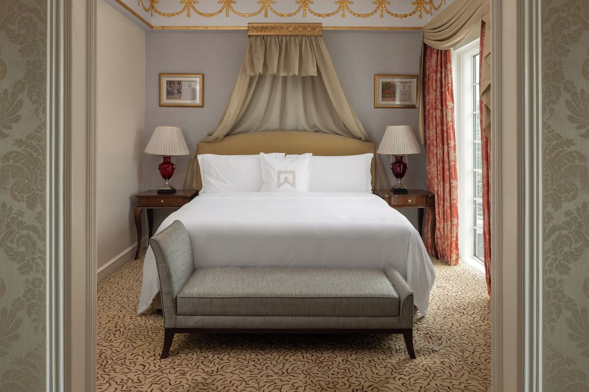 A hotel room with a large bed, two bedside tables with lamps, a bench, and patterned carpet.