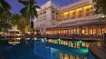 Surrounded by a lush garden with palm trees, the hotel's elegant architecture features a grand entrance and classical design elements.