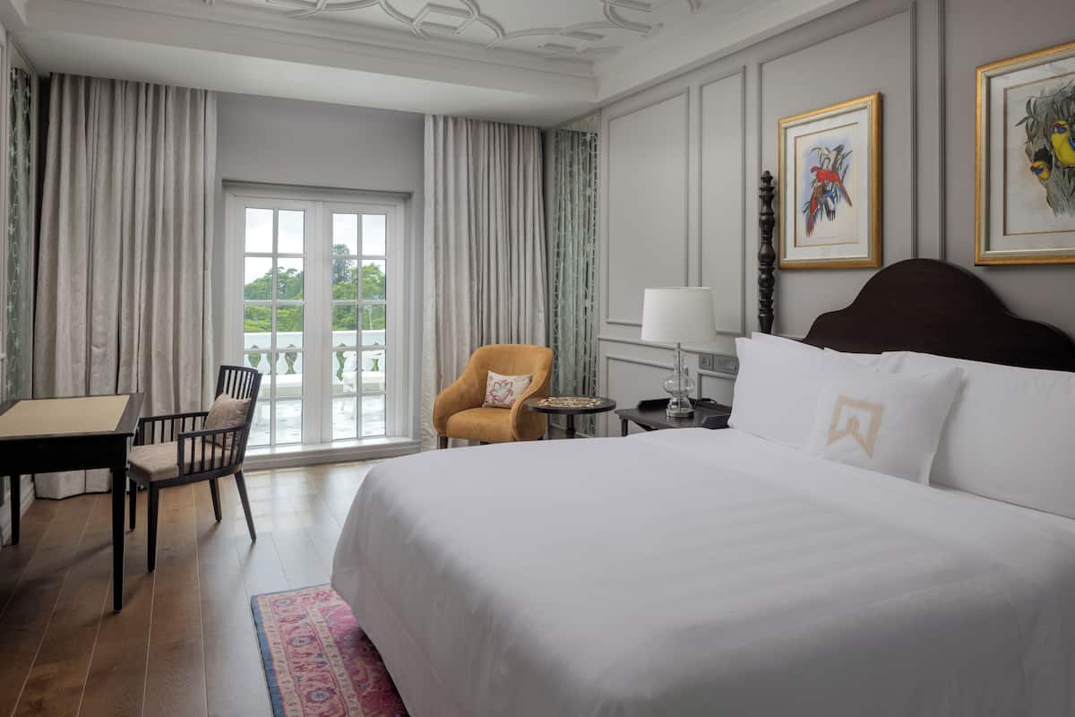 A hotel room with a large bed, a chair, a table, and a view of the outdoors through a window.