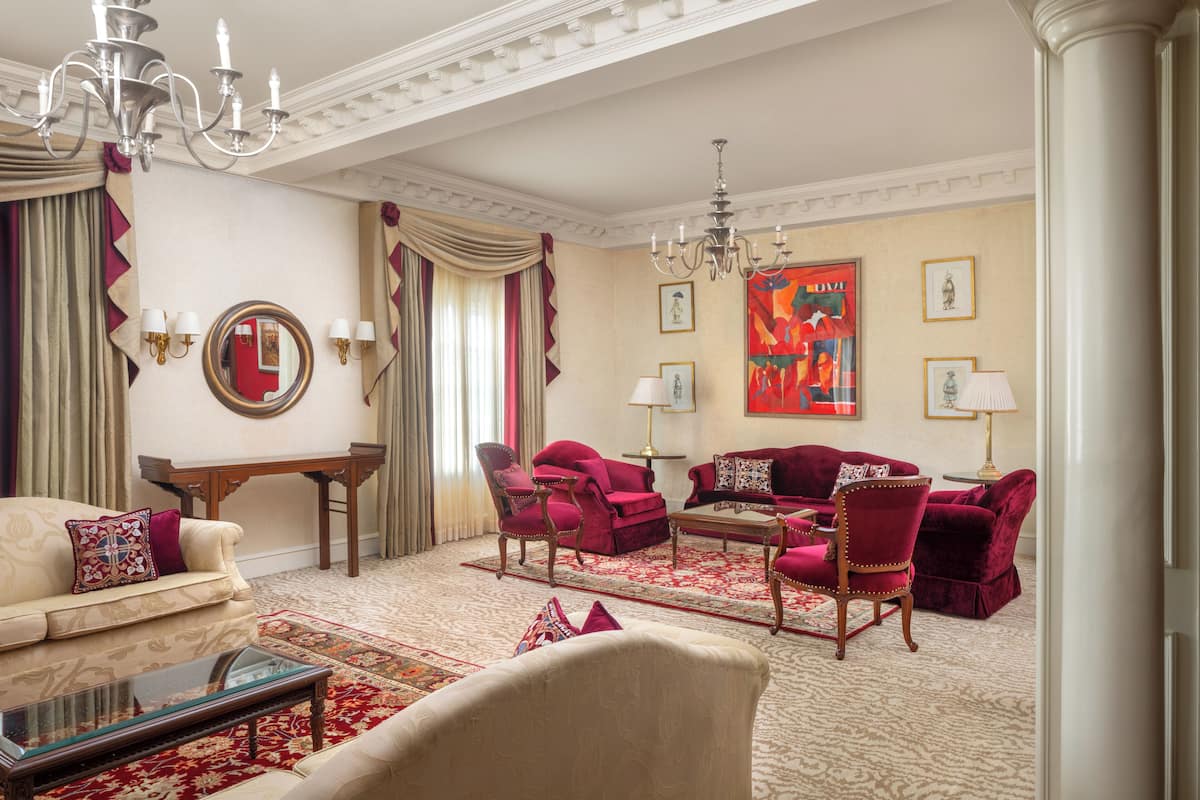 A luxurious living room with a chandelier, red and beige furniture, and a large painting on the wall.