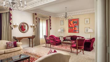 A luxurious living room with a chandelier, red and beige furniture, and a large painting on the wall.